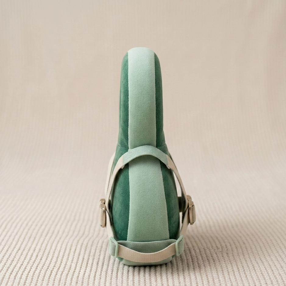 A mint green velvet shoe shown from the back, featuring a matching velvet heel counter and light beige leather straps with gold-tone hardware, set against a textured beige background.