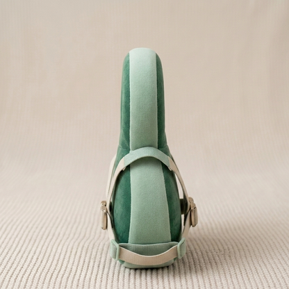 A mint green velvet shoe shown from the back, featuring a matching velvet heel counter and light beige leather straps with gold-tone hardware, set against a textured beige background.
